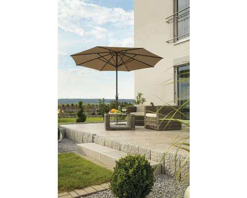 Scène de jardin avec parasol, table et fauteuils en rotin sur une terrasse en pierre.