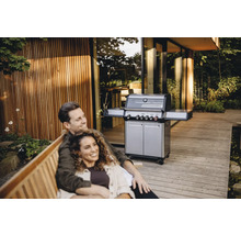 Couple se détendant sur un banc à l'extérieur avec un gril à gaz en arrière-plan.