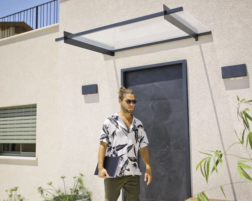 Marquise de porte moderne avec cadre en métal noir et panneau transparent au-dessus d'une entrée sombre sur une façade claire.