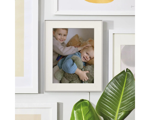 Cadre photo avec passe-partout et photo sur un mur de cadres à côté d'une plante d'intérieur.