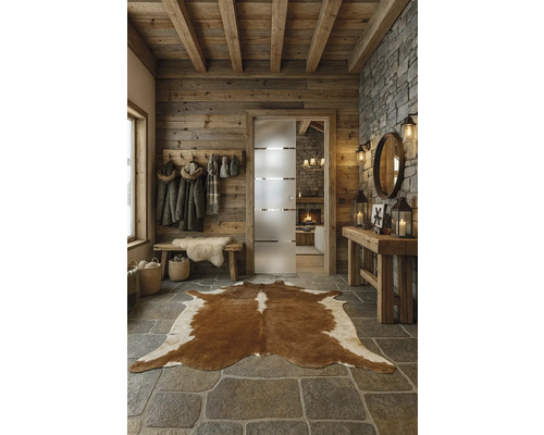 Rustikaler Eingangsbereich mit Holzwand, Steinboden und Kuhfellteppich.