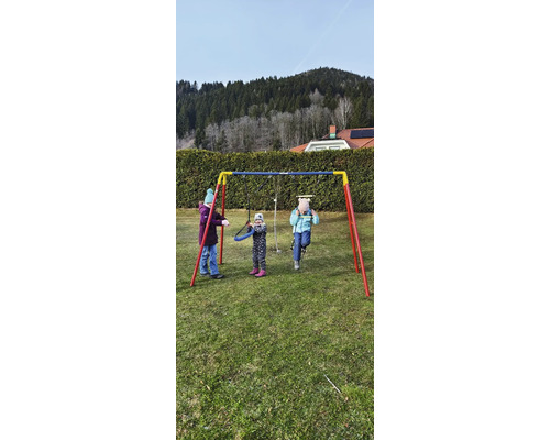 Scène avec trois enfants jouant sur une balançoire en métal dans le jardin