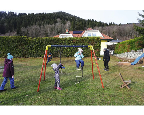 Des enfants jouent sur une balançoire Kettler dans le jardin.