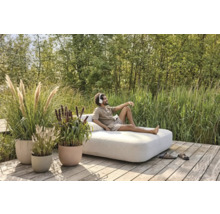 Un homme se détend sur un banc de jardin sur une terrasse en bois, entouré de graminées ornementales dans des jardinières