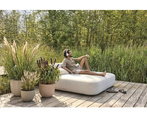 Un homme se détend sur un transat de jardin sur une terrasse en bois, entouré d'herbes et de plantes en pot.