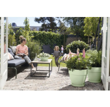 Scène de jardin avec une femme assise sur un banc, un enfant jouant et des pots de fleurs plantés sur une terrasse.