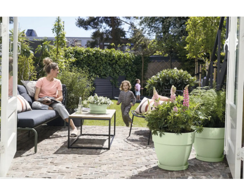 Scène de jardin avec une femme assise sur un banc, un enfant jouant et des pots de fleurs plantés sur une terrasse.
