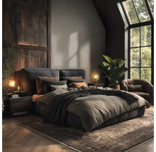 Schlafzimmer mit Doppelbett, Nachttischen, Lampen, Sessel, Zimmerpflanze und Teppich.