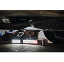 Une personne est allongée sous une voiture et utilise une lampe de travail pour les réparations.