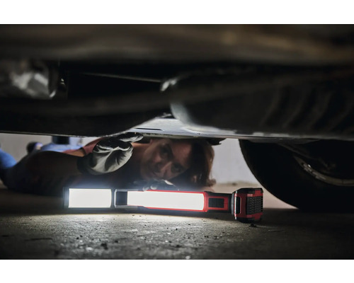 Une personne est allongée sous une voiture et utilise une lampe de travail pour les réparations.