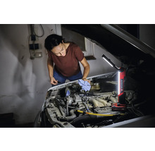 Femme vérifie le niveau d'huile d'une voiture avec une lampe à batterie Einhell