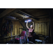 Femme installant une lampe LED dans un garage en bois, outils et chaises à l'arrière-plan