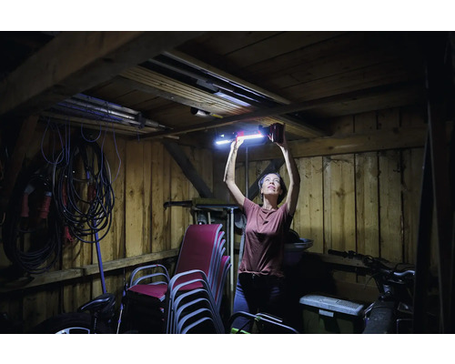 Femme installant une lampe LED dans un garage en bois, outils et chaises à l'arrière-plan