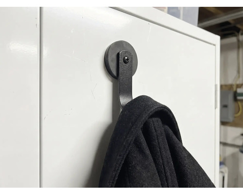 Patère magnétique noire sur une surface blanche avec une veste suspendue