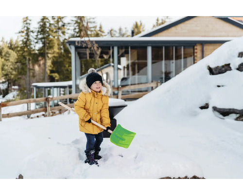 Un enfant avec une pelle à neige dans le jardin enneigé d'une maison