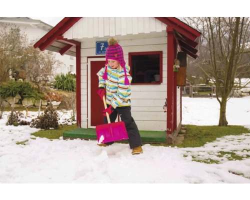 Fille pelletant la neige devant une cabane de jeu dans le jardin