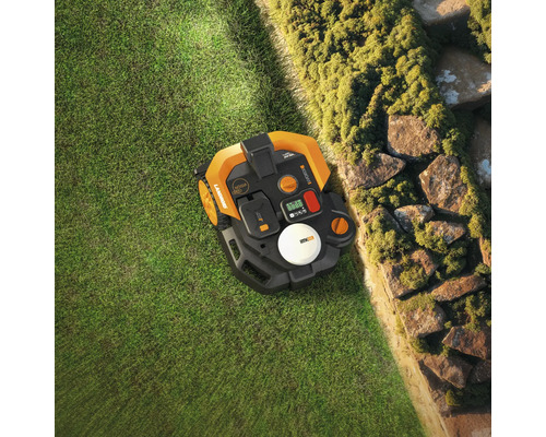 Vue de dessus d'un robot tondeuse sur une pelouse à côté d'un mur de pierre