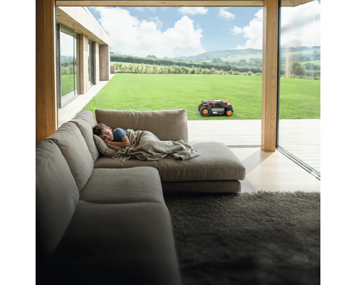 Szene mit Junge, der auf einem Sofa liegt, während ein Mähroboter im Garten arbeitet