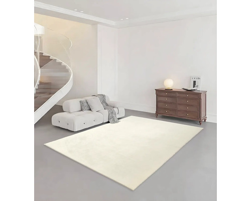 Salon lumineux avec tapis clair, canapé, commode et escalier en colimaçon.
