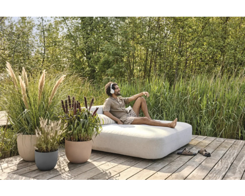 Szene mit Mann, der auf einem Sofa im Freien entspannt, umgeben von Pflanzen in Blumentöpfen auf einer Holzterrasse