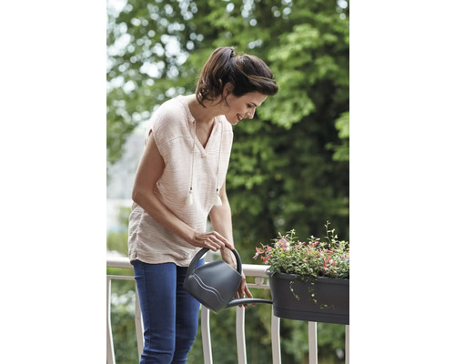 Une femme arrose des plantes dans une jardinière avec un arrosoir sur un balcon.