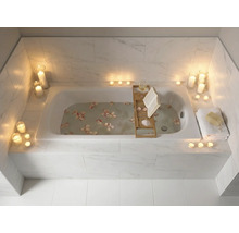 Badezimmer mit Badewanne, beleuchtet mit Kerzen und dekoriert mit Blütenblättern, mit Badewannenablage mit Buch und Glas
