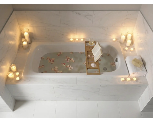 Badezimmer mit Badewanne, beleuchtet mit Kerzen und dekoriert mit Blütenblättern, mit Badewannenablage mit Buch und Glas