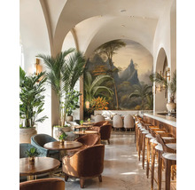 Espace bar lumineux avec arches, fresque tropicale, meubles en bois, fauteuils en velours et grands palmiers d'intérieur.