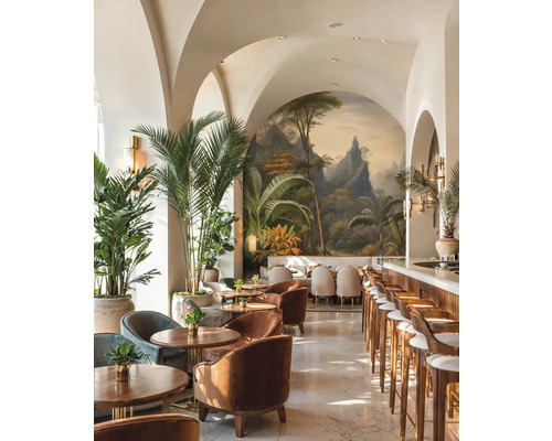 Espace bar lumineux avec arches, fresque tropicale, meubles en bois, fauteuils en velours et grands palmiers d'intérieur.