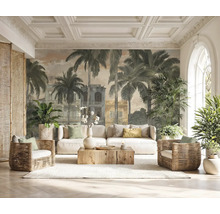 Papier peint panoramique avec palmiers et bâtiments coloniaux dans un salon lumineux avec canapé blanc, fauteuils en osier et table basse en bois.