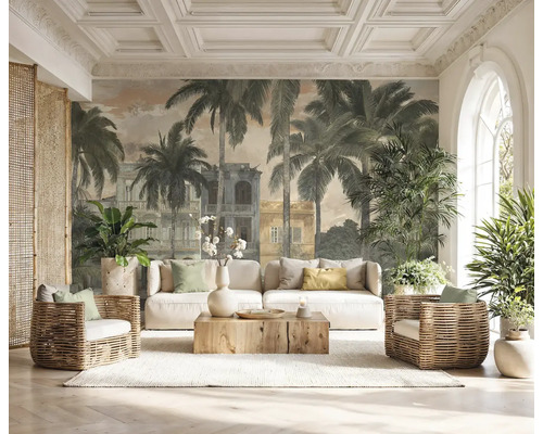 Papier peint panoramique avec palmiers et bâtiments coloniaux dans un salon lumineux avec canapé blanc, fauteuils en osier et table basse en bois.