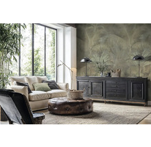 Salon moderne avec canapé clair, pouf en cuir et papier peint intissé avec motif de palmiers sur le mur derrière un buffet.