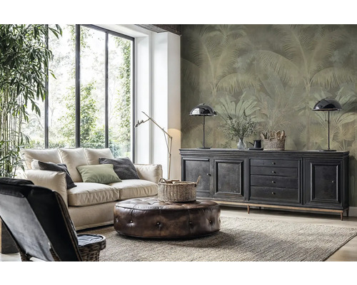 Salon moderne avec canapé clair, pouf en cuir et papier peint intissé avec motif de palmiers sur le mur derrière un buffet.