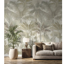 Papier peint intissé avec grand motif de palmiers dans un salon lumineux avec canapé beige, meubles en bois et une grande plante.