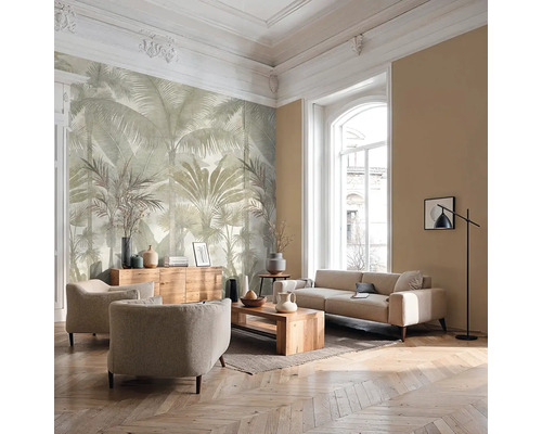 Salon lumineux avec papier peint panoramique motif palmiers, canapé, fauteuils, meubles en bois et parquet à chevrons.