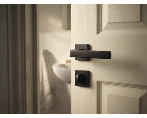 Tür mit schwarzer Türklinke und Badezimmer im Hintergrund