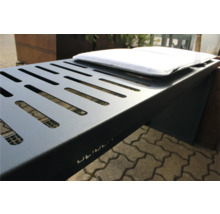 Detailansicht eines grauen Metallgrills mit Lüftungsschlitzen und weißem Kissen