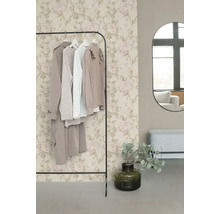 Papier peint intissé avec motif de roses romantique en beige et rose derrière un portant à vêtements dans un dressing moderne.