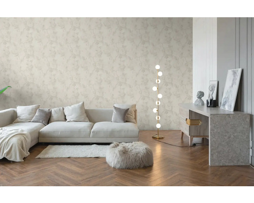 Salon lumineux avec papier peint intissé à motif floral, parquet en bois à bâtons rompus, canapé moderne et lampadaire.