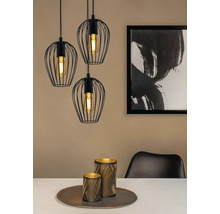 Trois suspensions noires avec abat-jour en fil de fer au-dessus d'une table à manger avec décoration