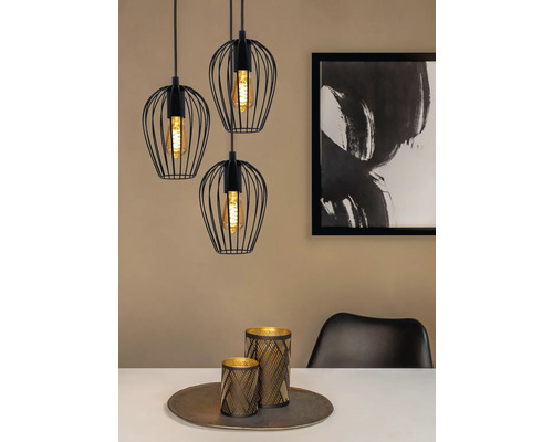 Trois suspensions noires avec abat-jour en fil de fer au-dessus d'une table à manger avec décoration