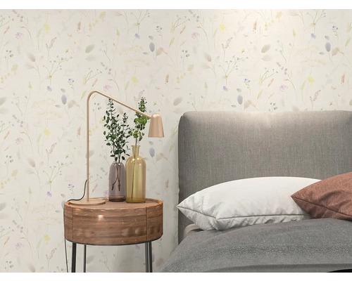 Helles Schlafzimmer mit floral gemusterter Tapete, grauem Polsterbett, rundem Nachttisch aus Holz und moderner Tischlampe aus Metall.