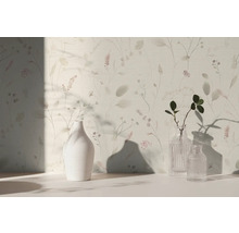 Helle Tapete mit filigranem Blumenmuster und Gräsern, davor stehen eine weiße Keramikvase und zwei Glasvasen auf einer hellen Fläche.