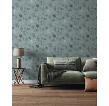 Scène de salon avec papier peint à motif de palmiers, canapé vert avec coussins et plaid, petite table en bois avec lampe et parquet.