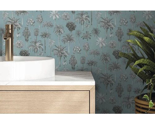 Papier peint à motif palmiers derrière une vasque blanche, robinet doré et meuble en bois dans une salle de bain moderne.