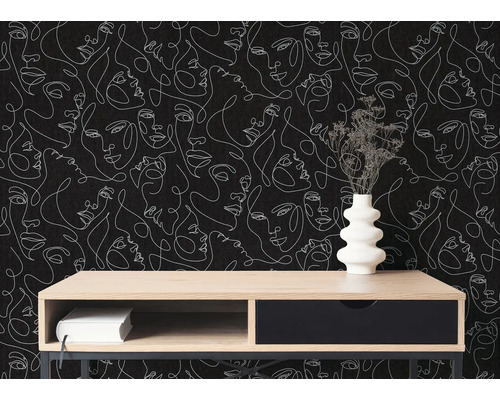 Moderne Inneneinrichtung mit Tapete im One-Line-Art-Design mit weißen Gesichtern auf schwarzem Grund. Davor ein Sideboard aus Holz mit Vase.