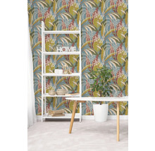 Vliestapete mit botanischem Blattmuster in Grün und Braun auf blauem Hintergrund, weißes Regal und Holztisch in hellem Raum.