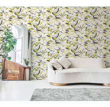 Papier peint intissé à motif de feuilles botaniques noir et jaune derrière un canapé crème dans un salon lumineux.