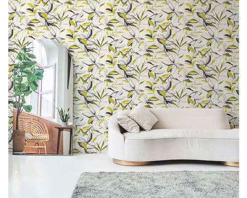 Papier peint intissé à motif de feuilles botaniques noir et jaune derrière un canapé crème dans un salon lumineux.