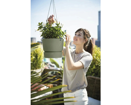 Frau betrachtet eine hängende Blumenampel mit weißen Blüten auf einem Balkon